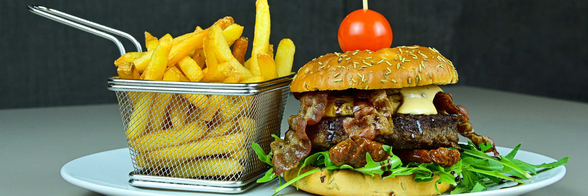 Luisenhof-Burger vom Angusrind, belegt mit Ziegenkäse, Bacon, getrockneten Tomaten und frischem Rucola, dazu Pommes frites
